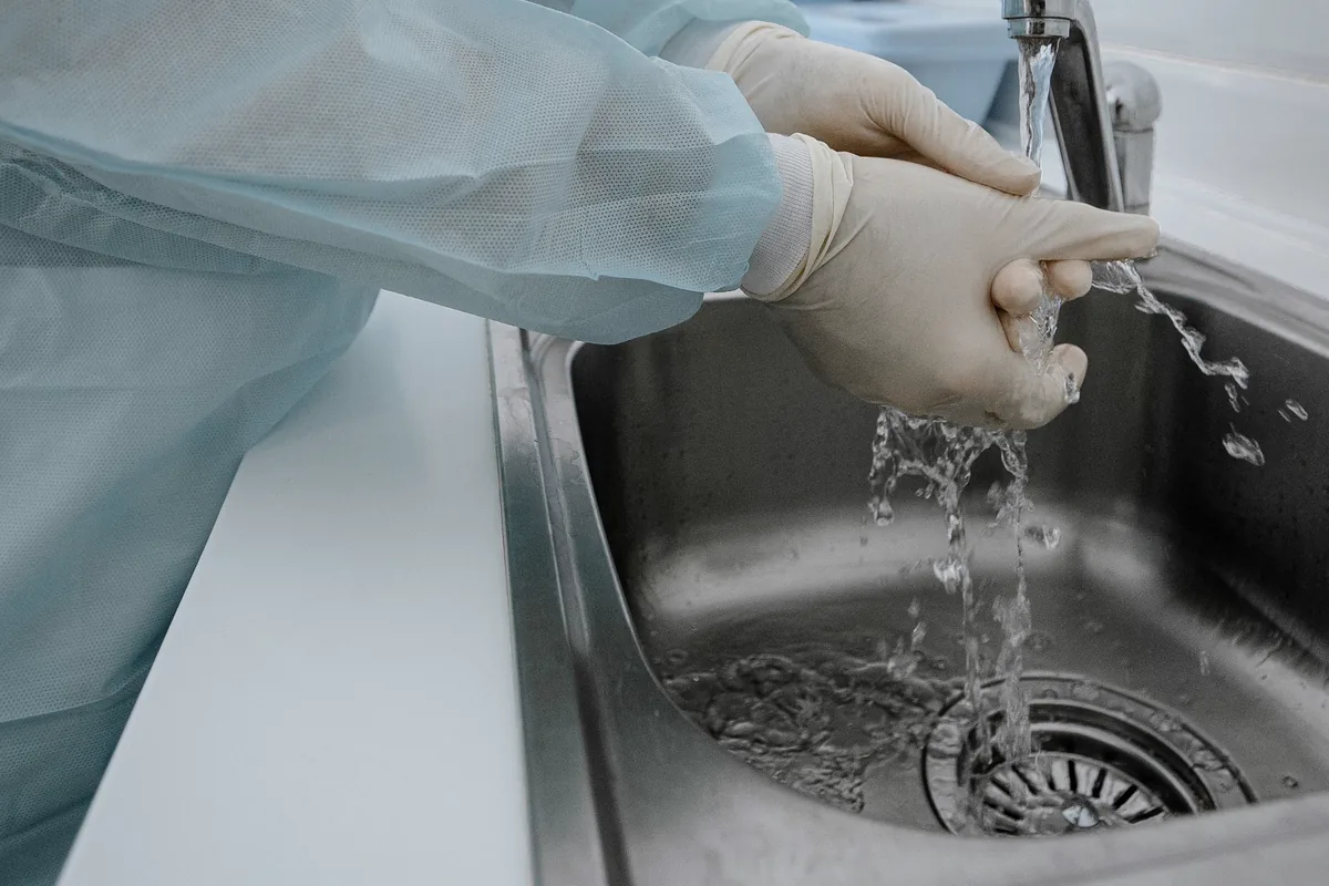 Mani con i guanti lavate sotto il rubinetto di un lavamani in acciaio inox